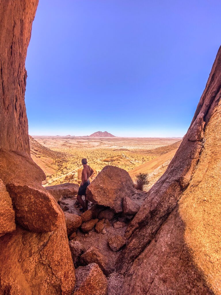 Person standing among large rock formations overlooking a wide desert landscape under a clear blue sky